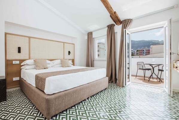 Habitación de hotel con una cama grande, cabecera de madera, balcón con mesa y sillas, y suelo con diseño.