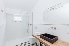 A modern bathroom with a glass-enclosed shower, a wooden vanity with a black sink, and a white toilet.