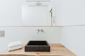 A modern bathroom with a rectangular black sink, white tiled walls, and a wooden countertop.