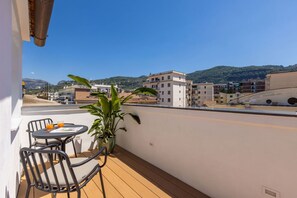 A balcony with a table and chairs, a potted plant, and a view of buildings and hills.
