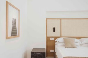 A hotel room with a bed, a nightstand, a framed picture on the wall, and a textured headboard.