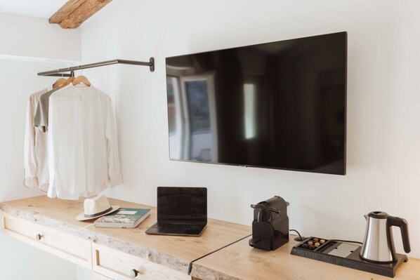 A modern room with a wooden desk, a laptop, a kettle, and a TV mounted on the wall.
