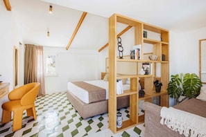 Ein Hotelzimmer mit einem Bett, einem Holzregal, einem Schreibtisch, einem orangefarbenen Sessel und einer Topfpflanze.