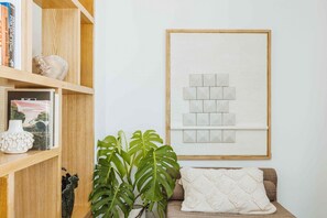 A living room with a bookshelf, a framed abstract art piece, a plant, and a sofa with a throw pillow.