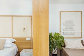 Ein Hotelzimmer mit einem Holzkopfteil, einem Bett mit weißer Bettwäsche, einem Marmornachttisch, einer Topfpflanze und einem gerahmten Kunstwerk an der Wand.