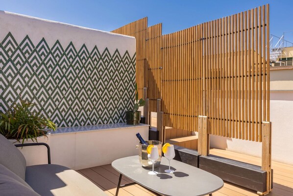 A rooftop terrace with a patterned wall, a wooden fence, a table with drinks, and a seating area.