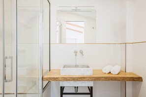 Un bagno con box doccia in vetro, lavabo in marmo e piano d'appoggio in legno.