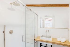 Ein modernes Badezimmer mit einer Duschkabine aus Glas, einem Holzkosmetikschrank mit Marmorbecken und einem Spiegel über dem Becken.