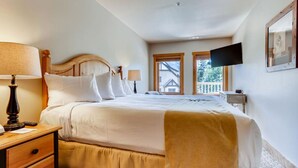Un letto rifatto con lenzuola bianche e una coperta beige, un comodino in legno con una lampada e un tavolino anch'esso con una lampada.