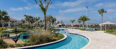 A pool area with a curved design, surrounded by palm trees and lounge chairs.