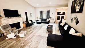 A modern living room with a fireplace, a flat-screen TV, and a large painting of a lion. - Spacious 6-bdrm luxury, modern house with lake view in cottage country, Ontario (Victoria Harbour)