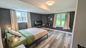 A modern bedroom with a bed, bedside lamps, a TV, and a window with curtains. - Spacious 6-bdrm luxury, modern house with lake view in cottage country, Ontario (Victoria Harbour)