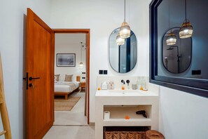 A modern bathroom with a large mirror, two pendant lights, a white sink, and a shower area. - Villa Flambard (Canggu)