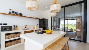 A modern kitchen with a central island, built-in wicker baskets, and hanging wicker pendant lights. - Villa Flambard (Canggu)