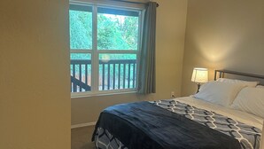 A bedroom with a bed, a nightstand, a window with a view of greenery, and a ceiling light.