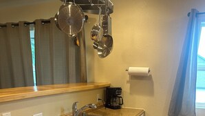 A kitchen with granite countertops, stainless steel sink, wooden cabinets, a coffee maker, and a dish rack.