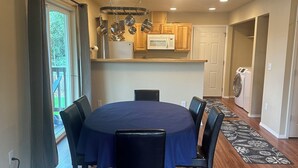 A dining area with a round table and chairs, a kitchen with wooden cabinets and a microwave, and a laundry area with a washing machine.