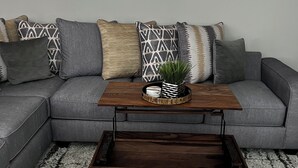 Un salon moderne avec un canapé d’angle gris, une table basse en bois et trois œuvres d’art abstraites encadrées accrochées au mur.