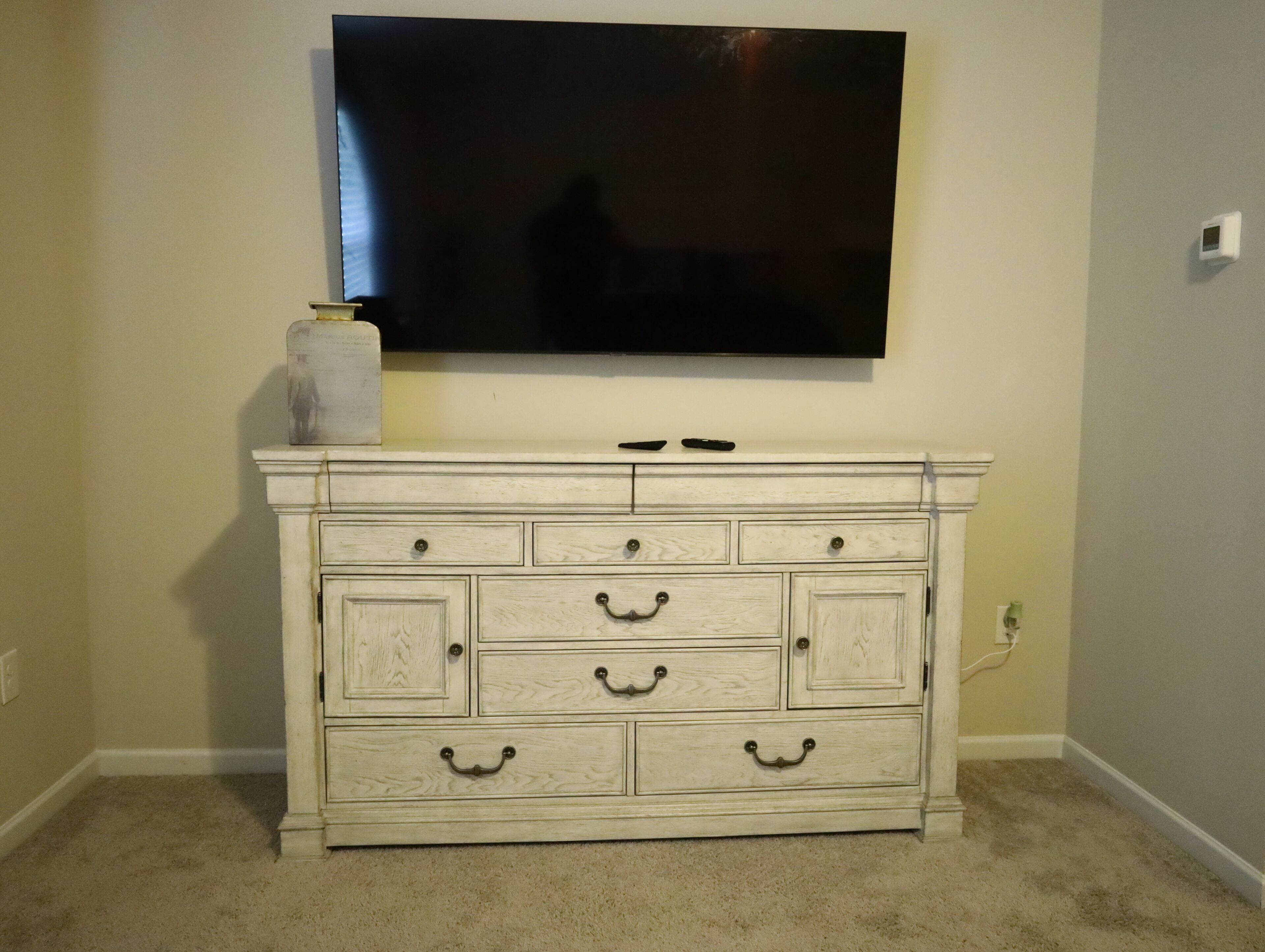Un aparador blanco con varios cajones y un televisor de pantalla plana montado encima.
