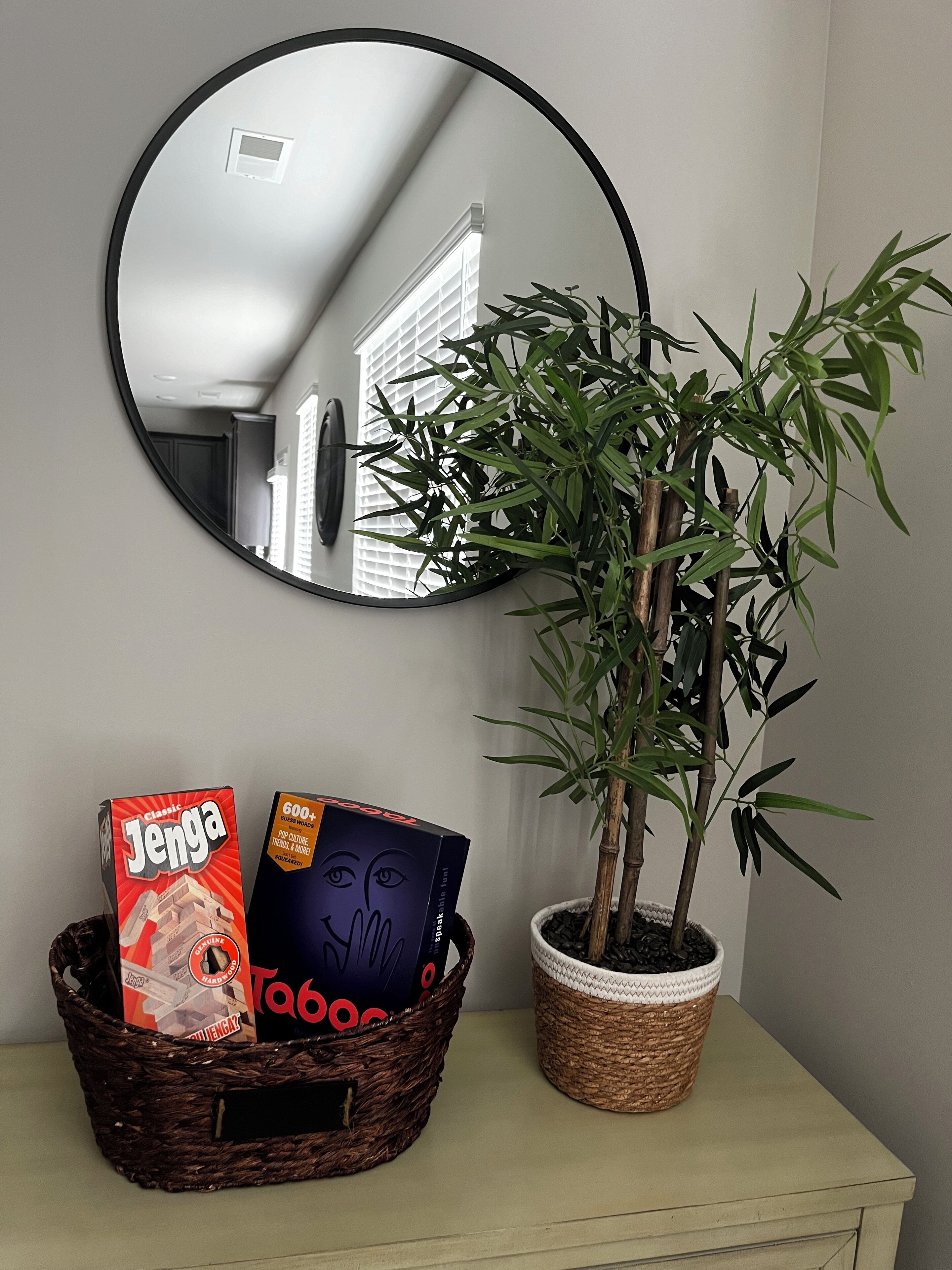 A room with a round mirror, a potted plant, and a wicker basket containing books.