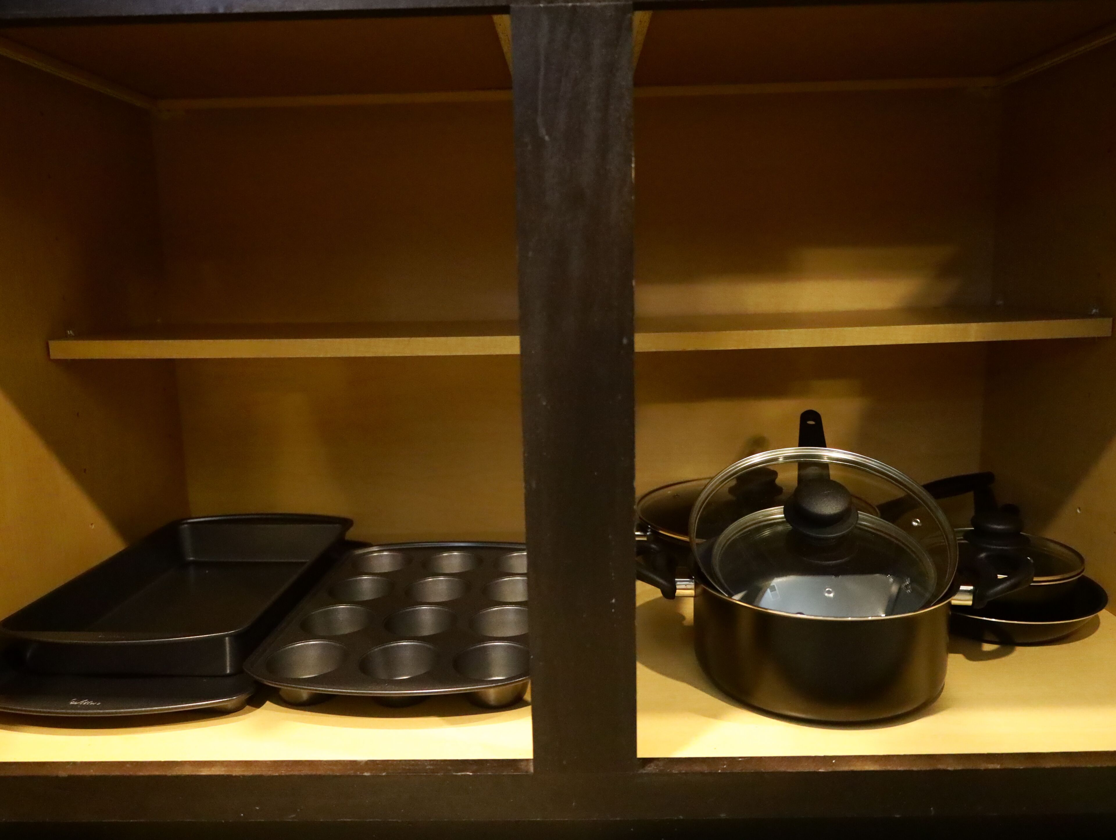 A kitchen shelf with a muffin tray, a pot with a lid, and a kettle.