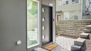 A modern entrance with a glass door, a small porch area, and a stone wall with steps leading up to a second-floor balcony. - Travelers Dream-Steps to Space Needle- Shared Backyard (Seattle)