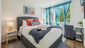 A neatly arranged bedroom with a bed, bedside table, lamp, and a desk with a chair. - Travelers Dream-Steps to Space Needle- Shared Backyard (Seattle)