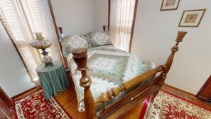 Una cama tradicional con dosel y doselera, un edredón floral, una mesita de noche de madera con lámpara y una alfombra roja estampada.