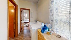 A laundry area with a washing machine, a drying rack, and a wooden cabinet with cleaning supplies.