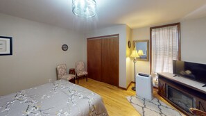 A bedroom with a bed, two chairs, a wardrobe, a television, a lamp, and a fireplace.