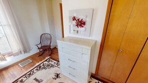 A room with a wooden floor, a white dresser with drawers, a rocking chair, and a wall-mounted artwork.