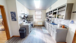 A compact kitchen with a stove, sink, and cabinets, a window with blinds, and a radiator.