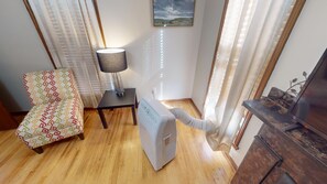 Una habitación con un sillón estampado, un calefactor portátil, una mesa con lámpara y un televisor sobre un soporte de madera.