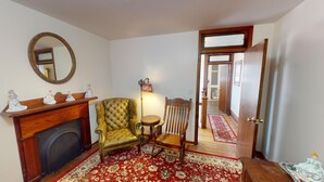 A room with a fireplace, a yellow armchair, a wooden chair, a mirror, and a door leading to another room.