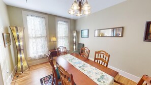 Un comedor con una mesa de madera, sillas, una araña y ventanas grandes con cortinas translúcidas.