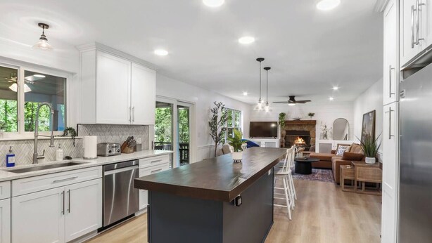 A modern kitchen with white cabinets, a central island, and a dining area with a fireplace. - Wildwood Retreat - Theater, Hot Tub and More! (Lake Geneva)