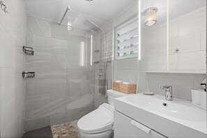 A modern bathroom with a shower, toilet, sink, and a mirror.