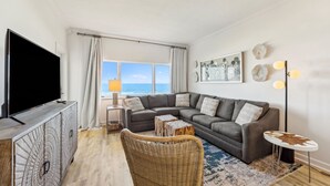 Una sala moderna con un sofá seccional, un televisor de pantalla plana, una silla de mimbre, una mesa de centro y una lámpara de pie.