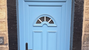 Eine blaue Tür mit schwarzem Griff und einem kleinen Blumentopf daneben.