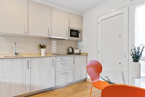 Una cocina moderna con armarios de madera clara, un microondas, un hervidor y una mesa de vidrio con una silla roja.