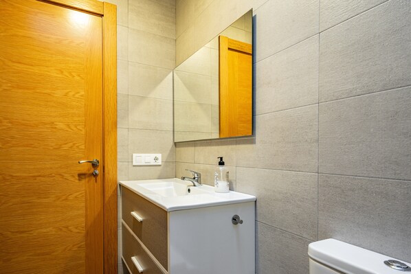A bathroom with a wooden door, a white sink, a mirror, and a toilet.