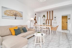 Un salon moderne avec un canapé, une table à manger et des chaises. Il y a un tableau au mur, une lampe et une plante en pot.