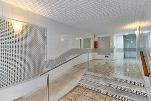 Un intérieur moderne avec un mur orné de motifs, un escalier doté d’une rampe en métal et un sol carrelé.