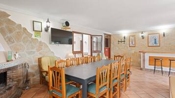 Un comedor con una mesa larga, sillas, una pared de piedra, una chimenea y una zona de bar.