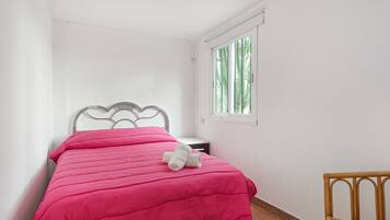 A small, neatly made room with a bed, a window, and a chair.