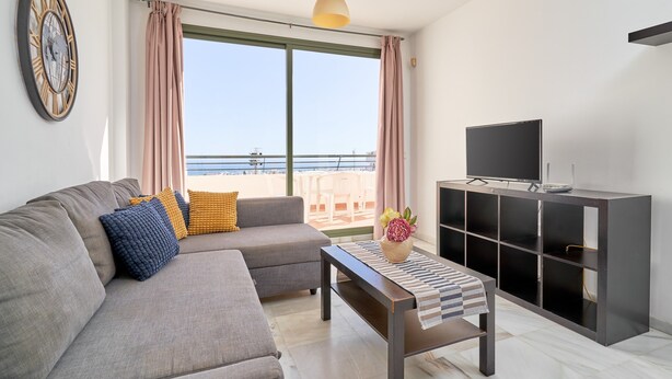 A living room with a sofa, a coffee table, a TV, and a balcony with a view. - Apartment 'Balcon De Nerja' with Sea View, Wi-Fi and Air Conditioning (Nerja)