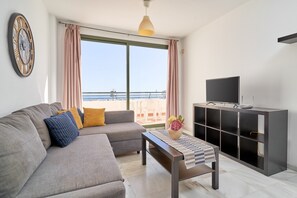Een woonkamer met een bank, een bijzettafeltje, een televisie en een balkon met uitzicht.