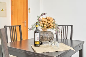 Une table à manger avec une bouteille de vin Shiraz, un vase contenant des fleurs séchées et deux verres à vin vides posés sur un set de table.