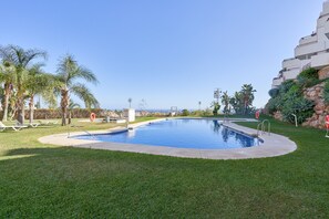 Une piscine entourée d’une pelouse, de palmiers et d’un bâtiment doté de balcons.