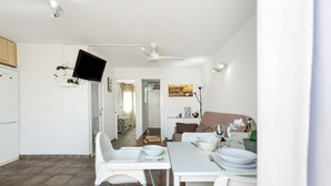 Een moderne keuken met witte apparaten, een eethoek met een gedekte tafel voor twee en een plafondventilator.